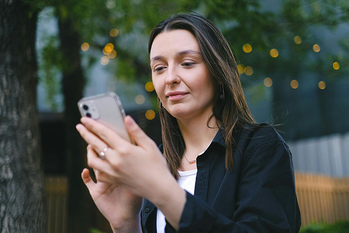 Woman using smartphone outdoors contemplating beauty lies