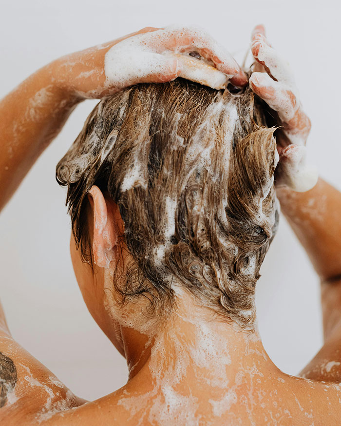 Person washing hair with shampoo lather close up beauty lies uncovered