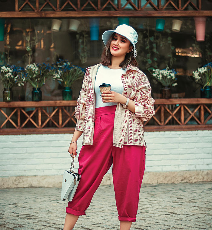 Fashionable woman in pink pants and hat holding coffee stylish beauty lies uncovered