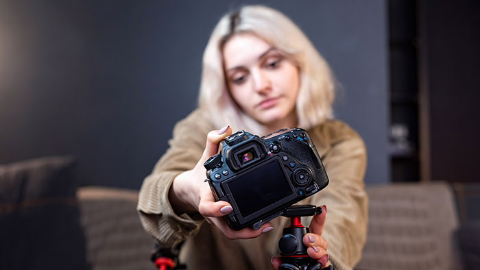 A woman with blonde hair in a brown shirt adjusts a camera on a tripod. This could relate to a "sister-in-law" dispute.