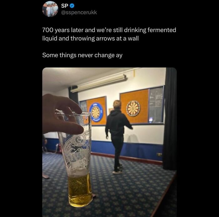 A British meme about tradition: a person holding a pint glass in the foreground, with another person playing darts.