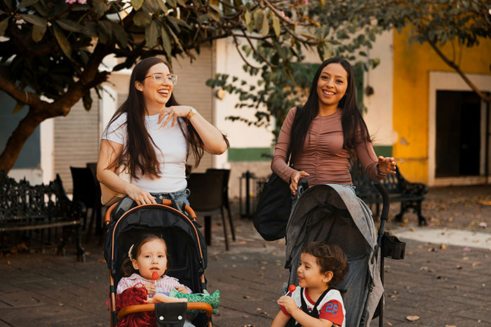 Two moms with three kids enjoying a sunny day with strollers in a park setting Two moms with three kids enjoying a sunny day with strollers in a park setting