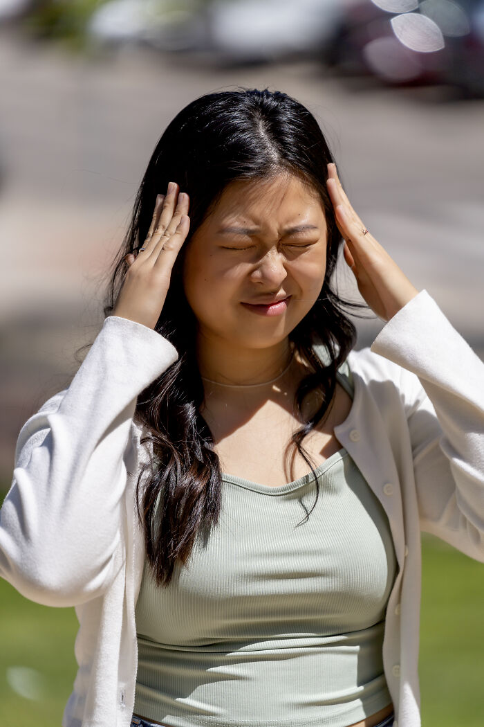 Young woman grimacing, holding her head, likely experiencing pain. Important for routine cancer screening awareness.