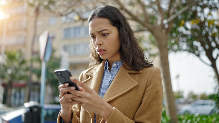 A young woman with a worried expression, looking down at her phone. Her expression indicates distress after breakups.