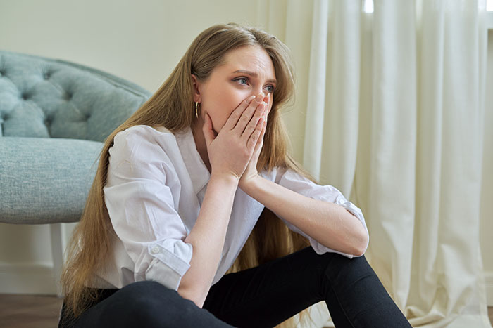 Stressed woman sitting on floor covering mouth contemplating sibling revenge