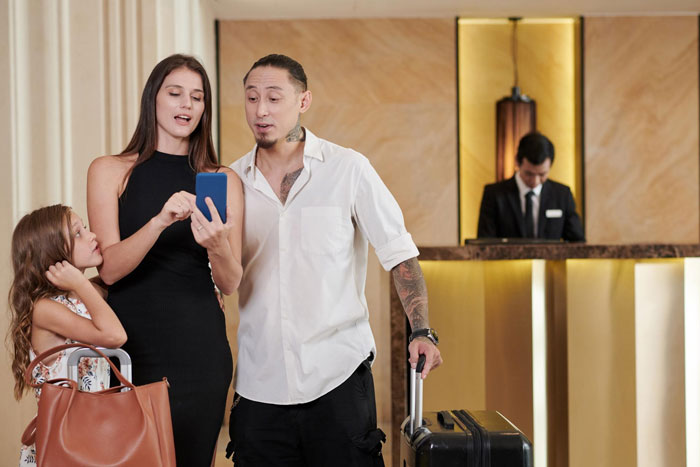 Family using phone and luggage at hotel reception desk Family using phone and luggage at hotel reception desk