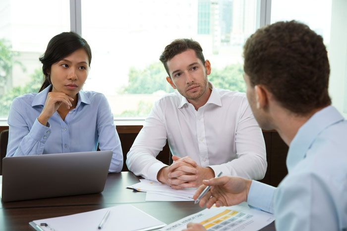 Business meeting with two professionals listening intently to colleague explaining documents Business meeting with two professionals listening intently to colleague explaining documents