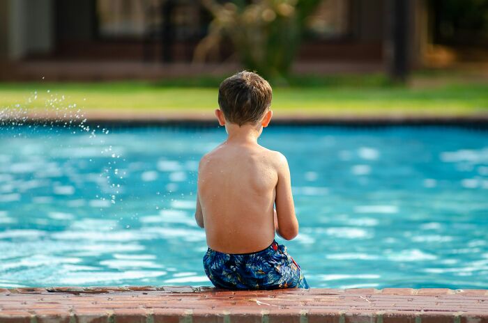 Boy sitting by pool with back turned and water splash