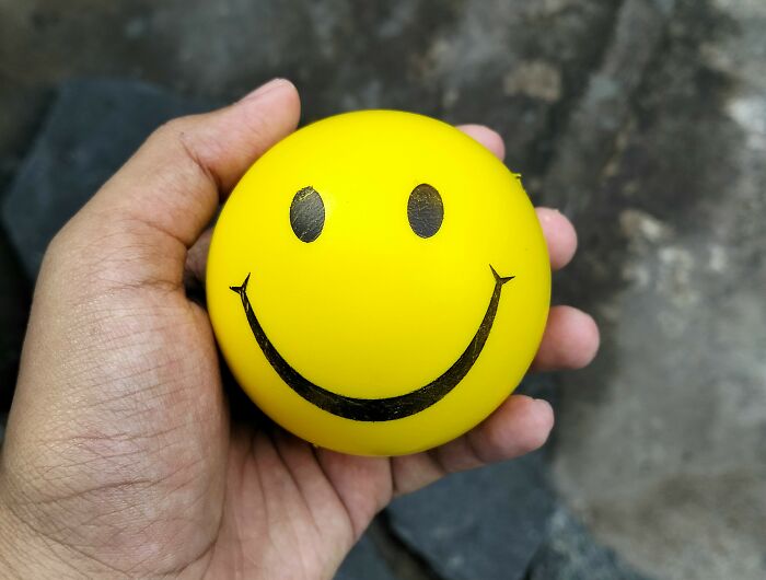 Hand holding yellow smiley face stress ball representing January 6 optimism
