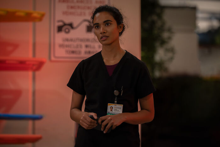 A woman in black scrubs with an ID badge looking concerned, highlighting The Pitt star's $750 a week salary confession.