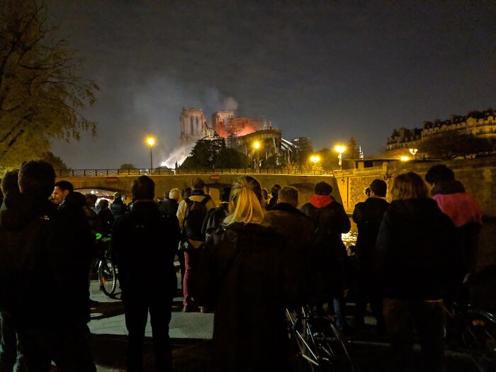 Crowd watching Notre Dame cathedral fire at night with flames and smoke