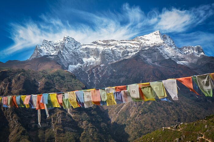 Snowy mountain with colorful prayer flags against bright blue sky geography facts