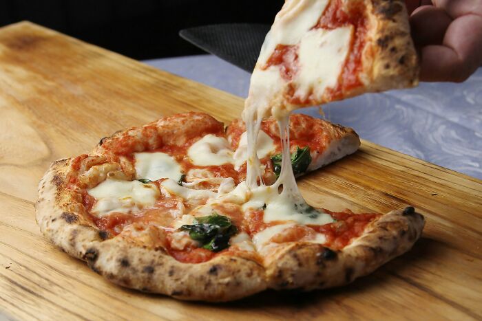 Slice of cheese pizza being lifted from whole pizza