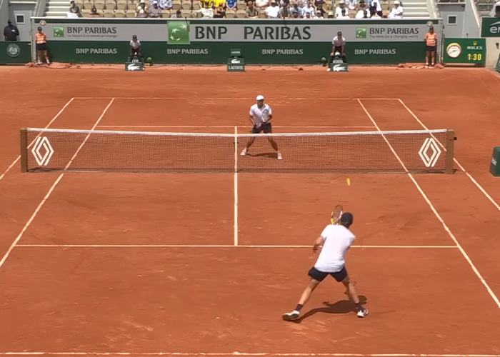 French Open tennis match on clay court with player preparing to return serve