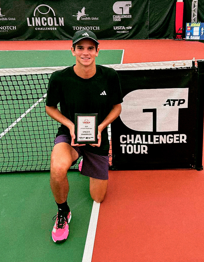Young tennis player kneeling with singles champion plaque at ATP Challenger event