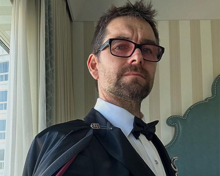 The Boys star posing in tuxedo and cape with glasses indoors The Boys star posing in tuxedo and cape with glasses indoors