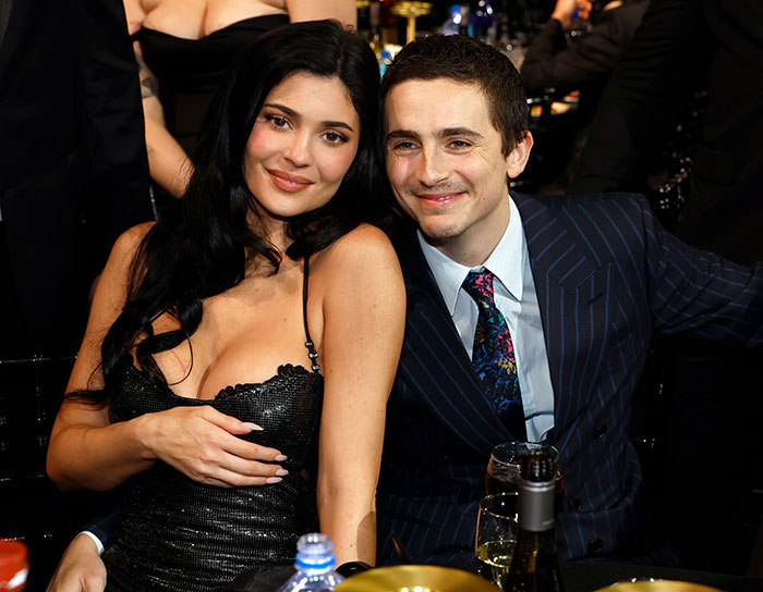 Timoth&eacute;e Chalamet and woman smiling together at formal manspreading event