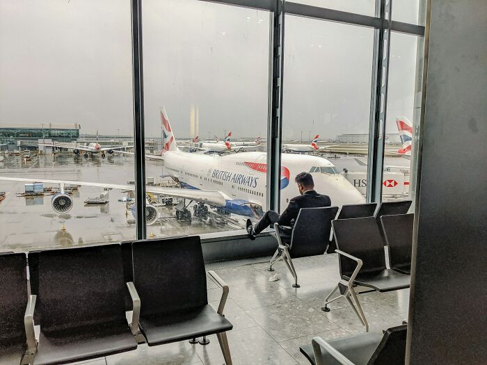 Man sitting in airport lounge with British Airways plane outside window