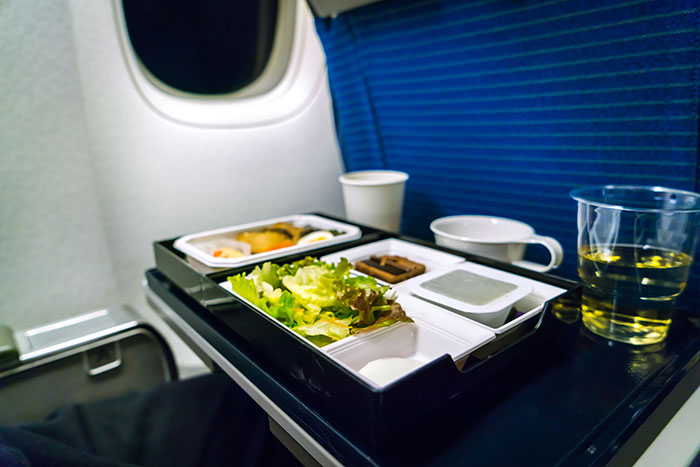 An airplane tray table holds an in-flight meal. A Karen might disapprove of someone eating meat on a flight.