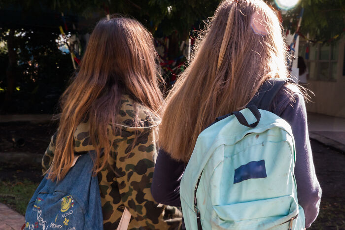 Two young people with long hair and backpacks, walking away. Habits deemed expensive can save money.