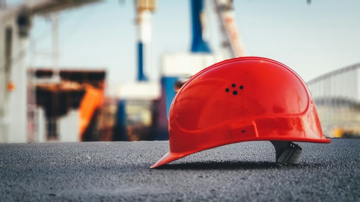 A red hard hat lies on asphalt, with a blurred industrial background. Symbolizes challenging cases lawyers defend.