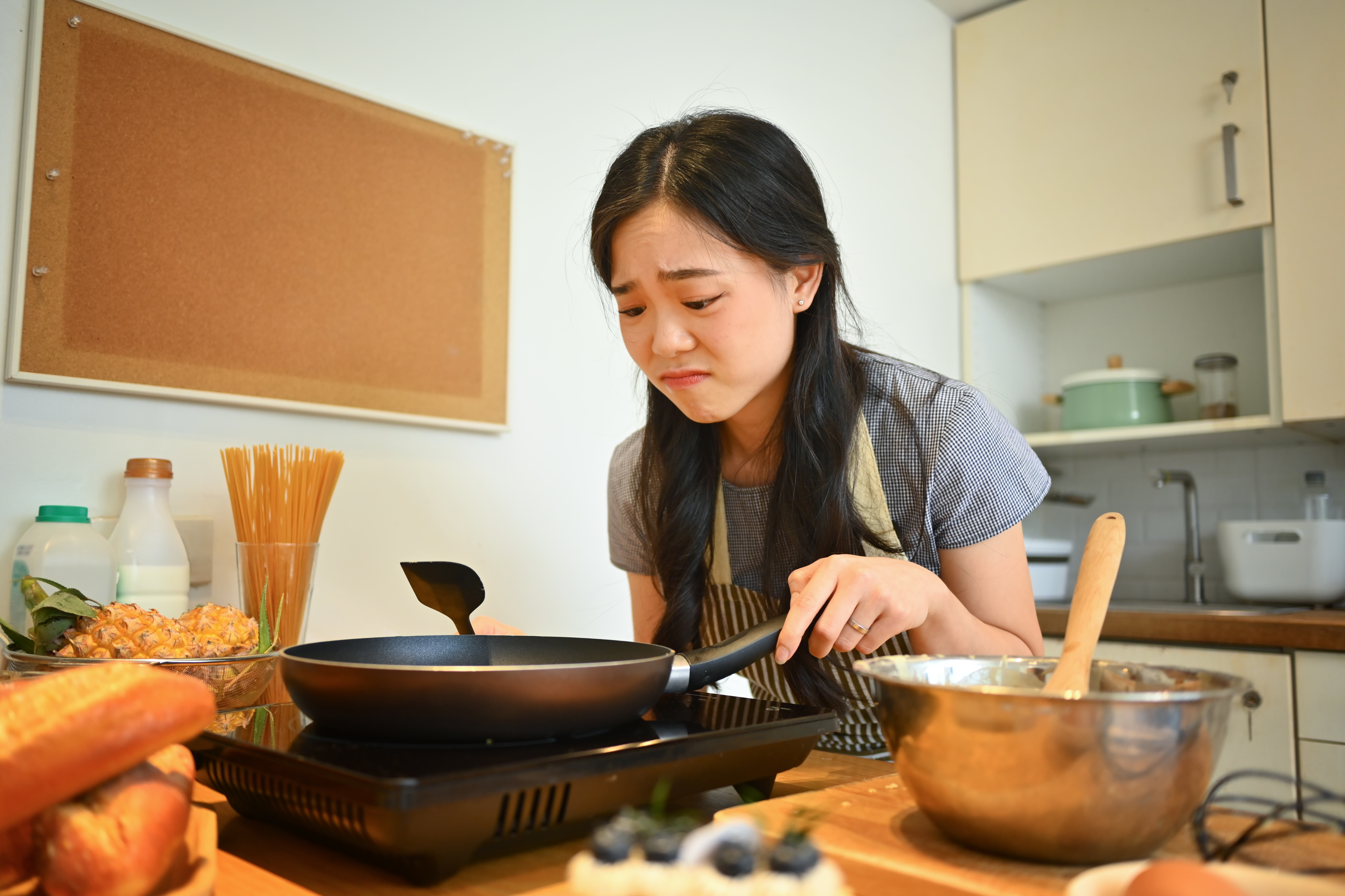 Woman looking disgusted and unhappy near stove cooking with frying pan