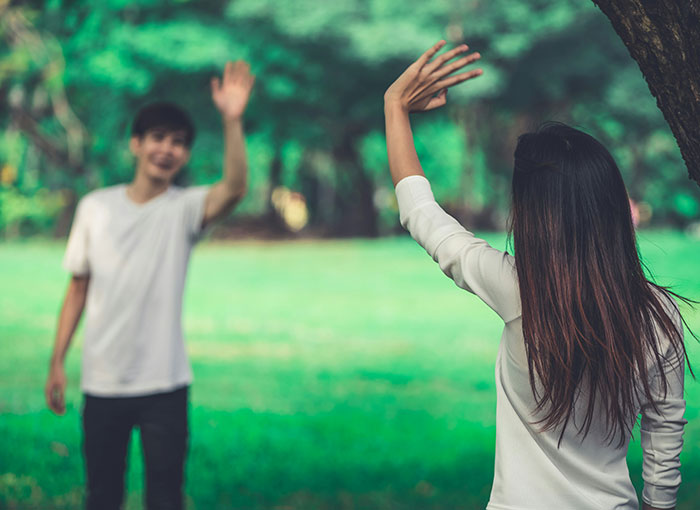 Two people waving to each other in a park, showing unspoken British rules of social interaction.