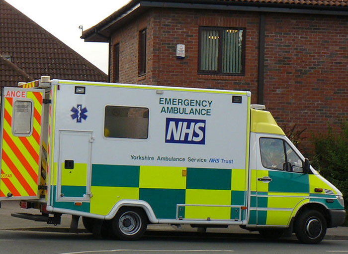 An NHS emergency ambulance, part of the Yorkshire Ambulance Service, parked near a brick building. Represents Brits unwritten rules.