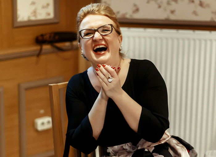 A laughing British woman with glasses and red nails, representing Brits sharing unwritten rules in their country.