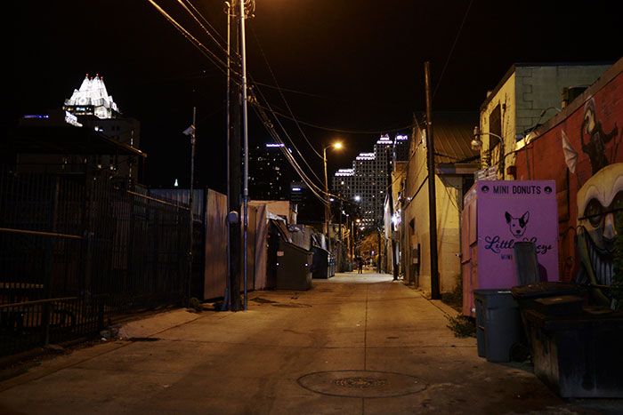 A dark alleyway at night with city lights in the background, representing US states.