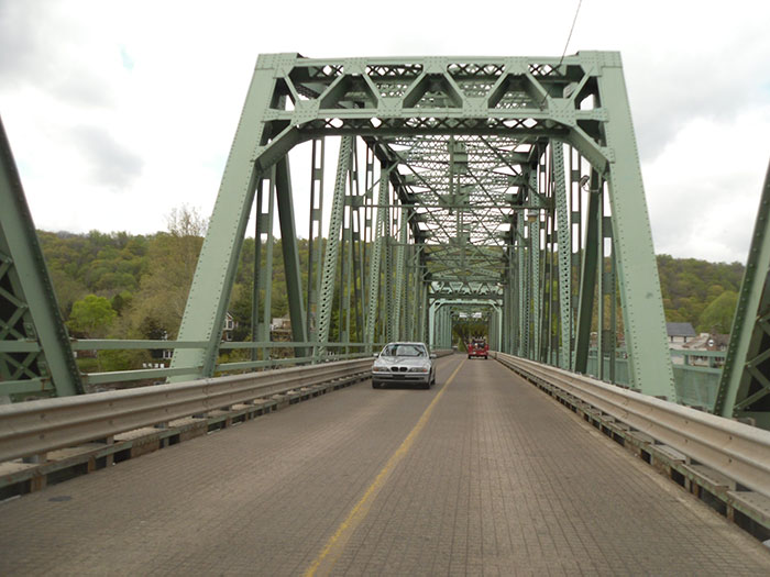 A sturdy green metal truss bridge with two cars driving on it, one silver and one red, representing US States.