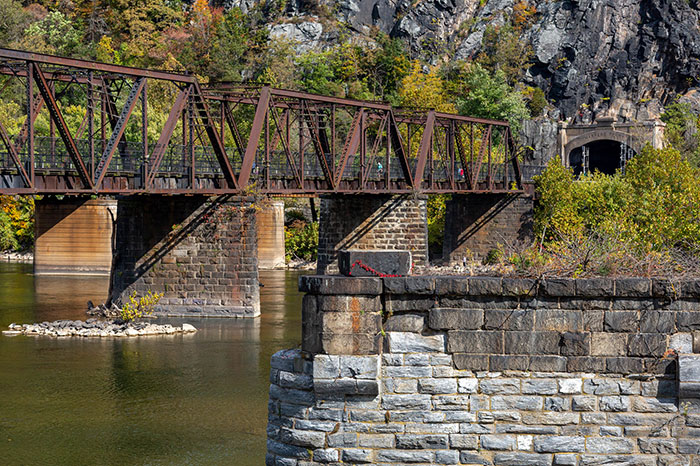 An old rusty railway bridge over a river with fall foliage, reflecting US states.