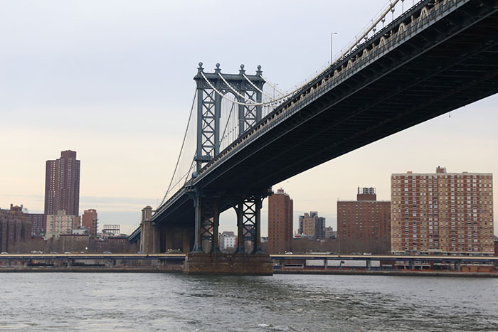 The majestic Manhattan Bridge spanning water with city buildings in the background, a sight from US states glorified in movies.