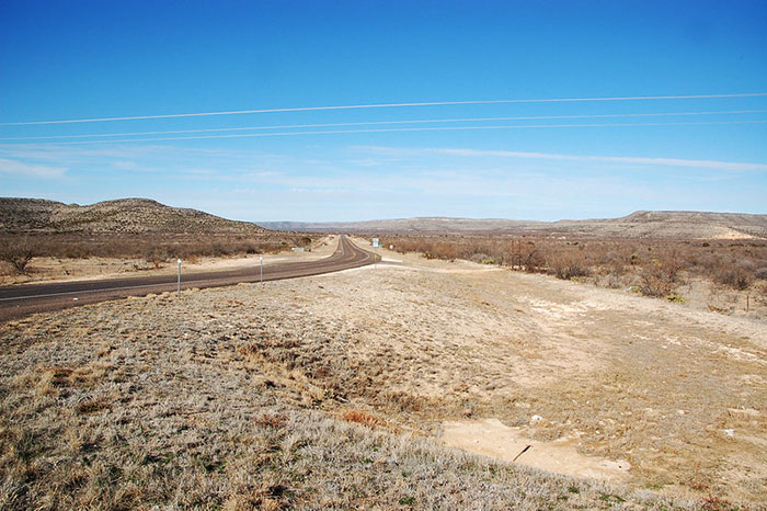 A long, winding road through a vast, barren desert landscape, indicative of US states glorified in movies.