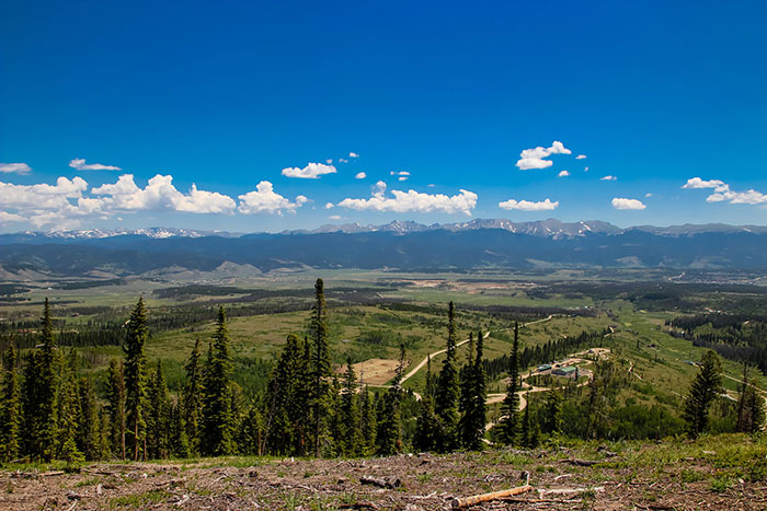 A sprawling mountain landscape with lush green forests and distant snow-capped peaks under a blue sky, characteristic of US States.