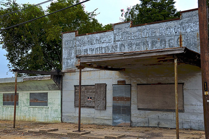 An abandoned, weathered building with boarded-up windows and a rusted awning, typical of neglected spots in US States.