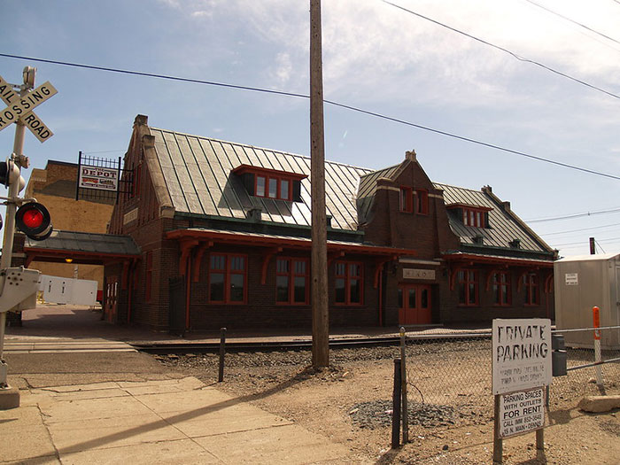 An old brick train station with a green roof, a classic structure found in many US States.