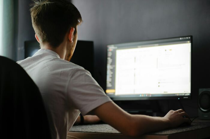 A man, seen from behind, sitting at a desk and using a computer mouse, illustrating manosphere content engagement.