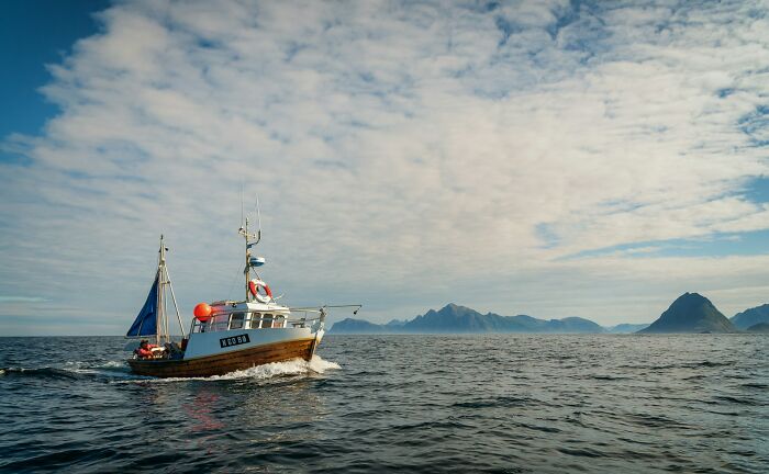 A small wooden fishing boat cuts through the ocean with mountains in the distance, a silent luxury many enjoy.