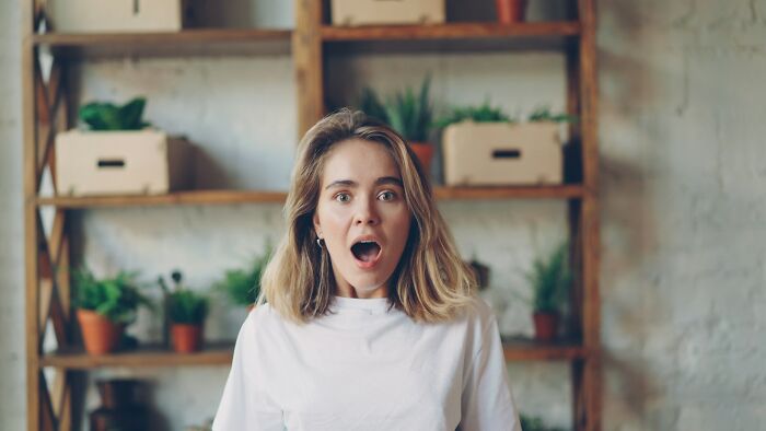 A surprised woman with her mouth open, in front of a wooden shelf with plants. This image illustrates engagement stories.