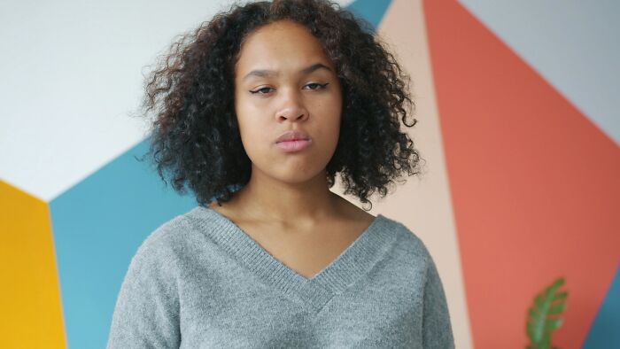 A young woman with curly hair and a grey sweater looking unimpressed, ready with an epic comeback.