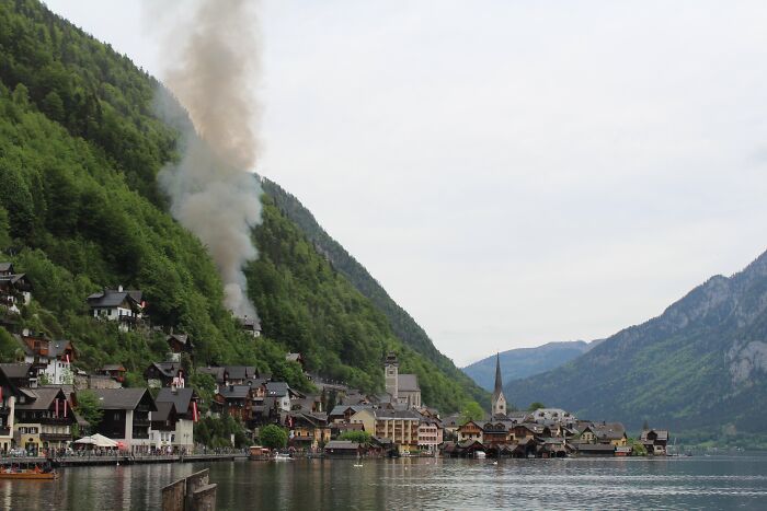 Rare smoke plume rising over quaint town by the lake surrounded by mountains
