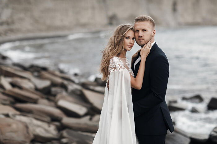 Couple in wedding attire posing at rocky seaside romantic wedding
