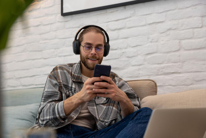 Man wearing headphones smiling and using smartphone at home