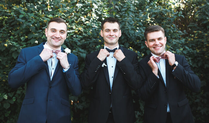 Three groomsmen adjusting bow ties outdoors