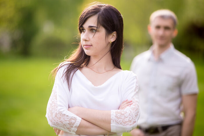 Woman crossing arms looking away with man blurred in background outdoors