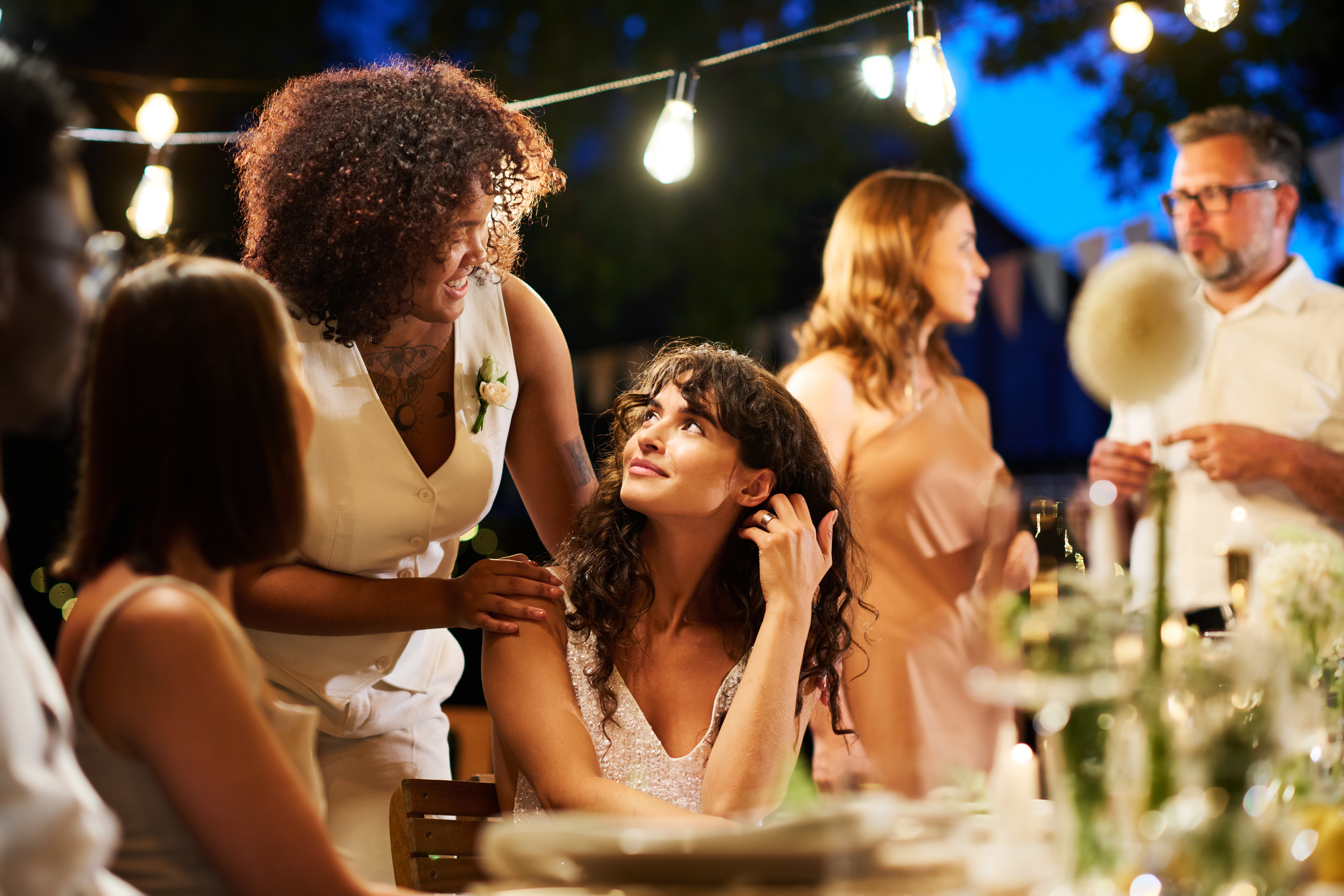 Women talking at a wedding reception amid string lights and evening setting Women talking at a wedding reception amid string lights and evening setting