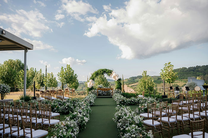An outdoor wedding venue with rows of chairs leading to a floral arch, overlooking a picturesque valley. #Wedding Moments