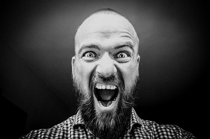Monochrome close-up of a bearded man screaming with wide eyes, expressing frustration about a marriage moment.