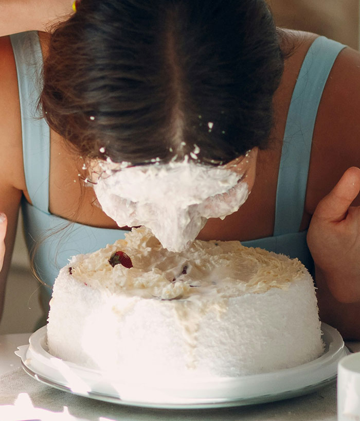 A woman's face covered in white frosting after smashing into a cake, showing a funny wedding moment.